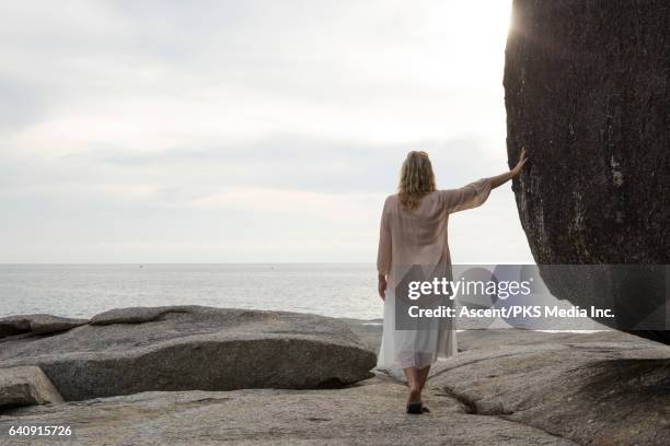 woman leans against rock boulder on rock slab, above sea - falda color crema fotografías e imágenes de stock