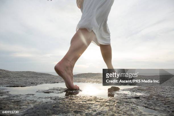 woman leaps across rock slab pool, above sea - barefoot foto e immagini stock