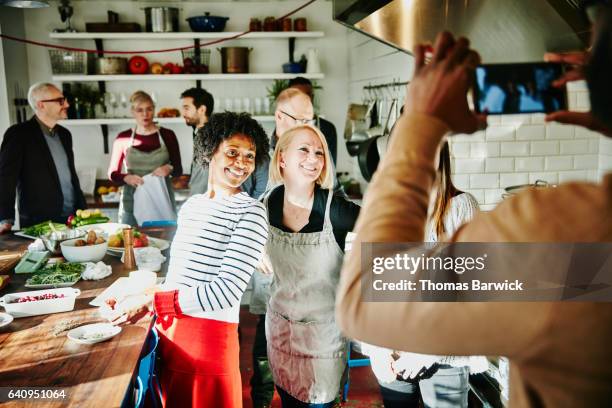 man taking a picture of smiling friends with smartphone during cooking class - frau mittleren alters stock-fotos und bilder