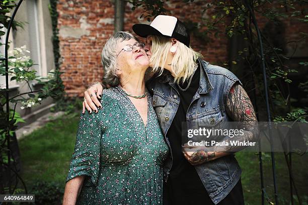 daughter kissing mother while standing in back yard - mutterliebe erwachsener sohn stock-fotos und bilder