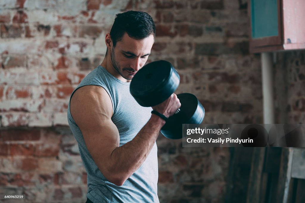 Determined young man lifting dumbbell at gym