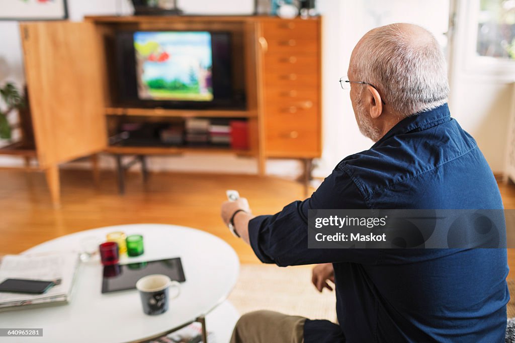 Rear view of senior man changing channels at home