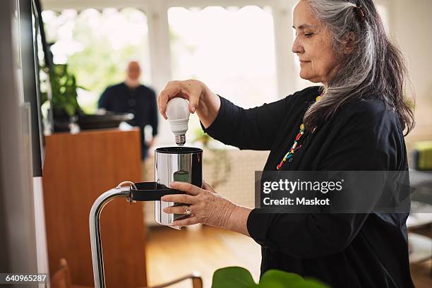 senior woman changing bulb at home - lampje-vervangen stockfoto's en -beelden