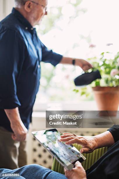cropped image of senior woman using digital tablet while man watering flower plant - doctoring stock pictures, royalty-free photos & images