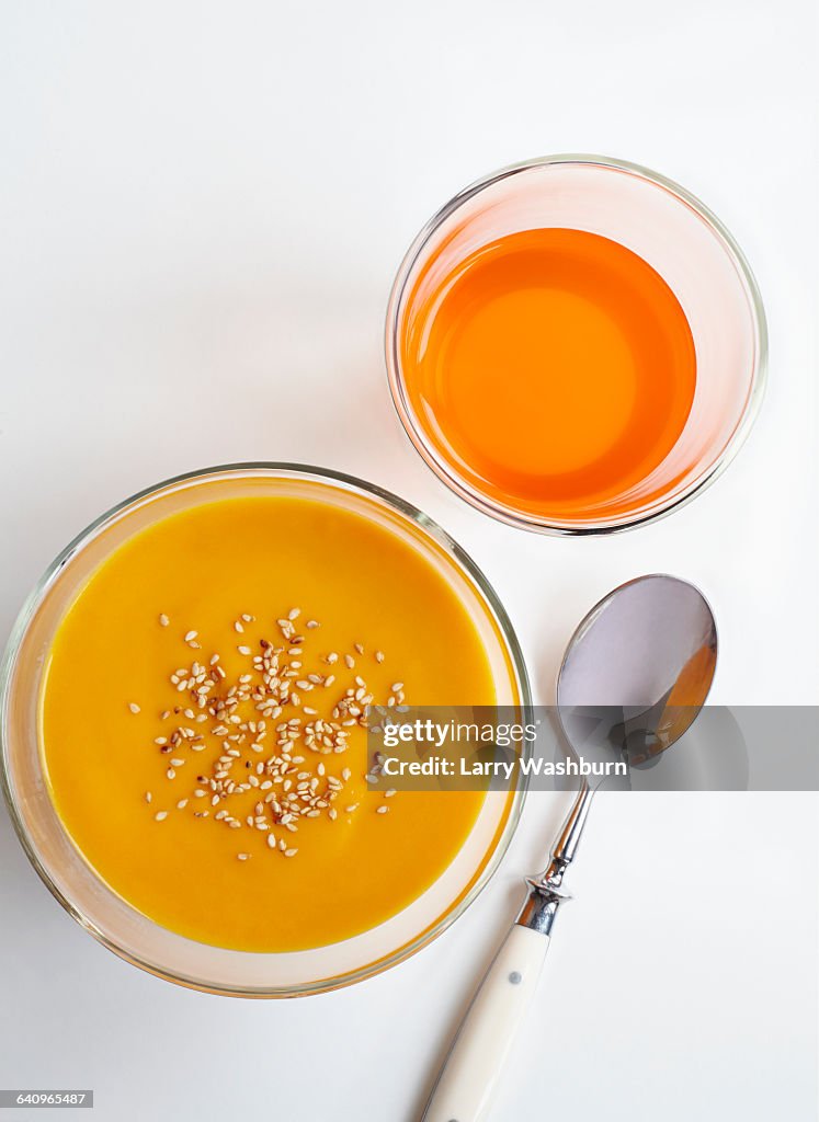 High angle view of carrot puree and drink with spoon over white background