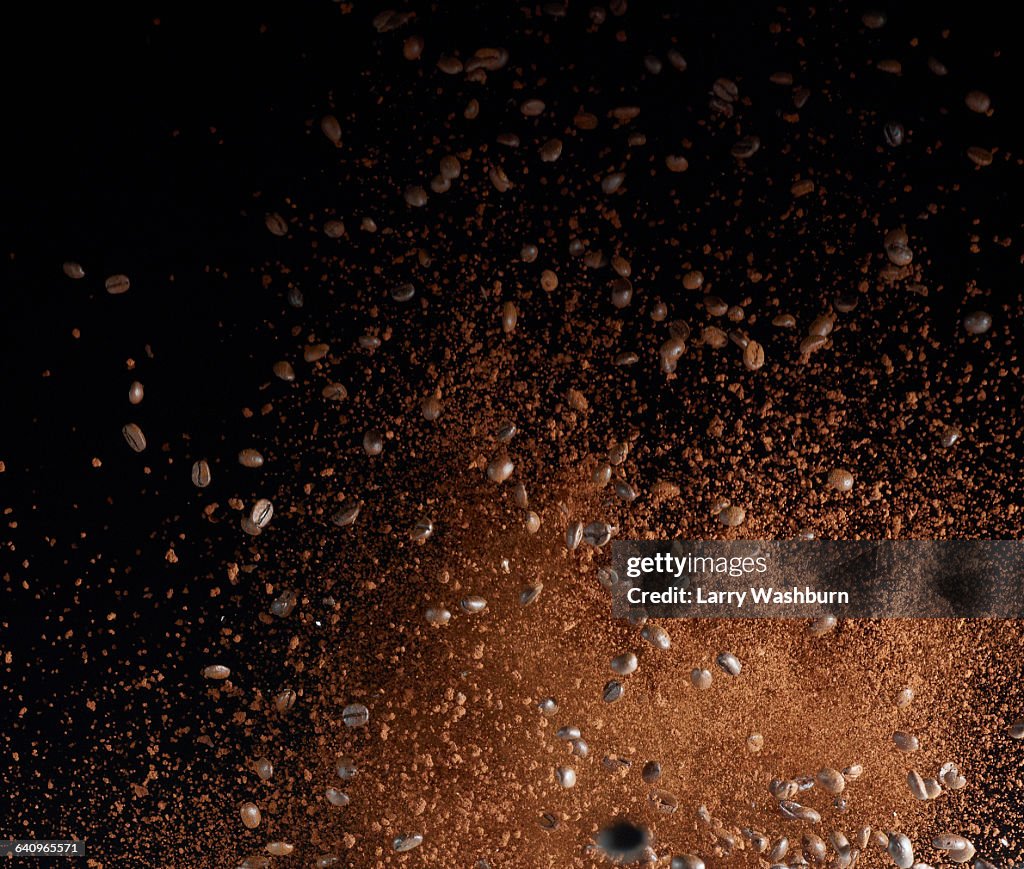 Ground coffee beans in mid-air against black background