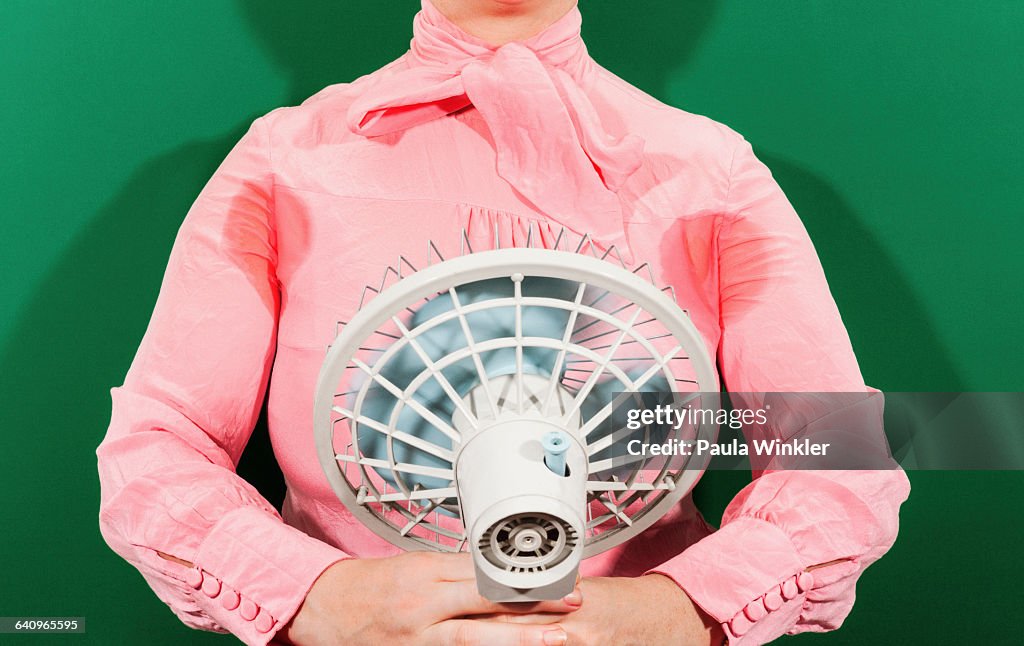 Midsection of businesswoman with sweaty armpits holding fan against green background