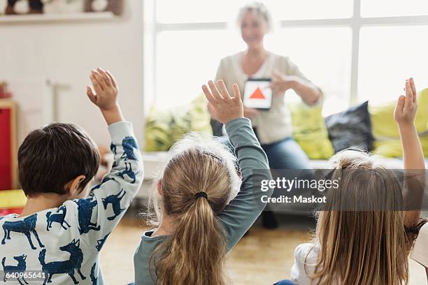 rear view of students raising hands while teacher showing digital tablet at preschool - 4 blond girls stock pictures, royalty-free photos & images