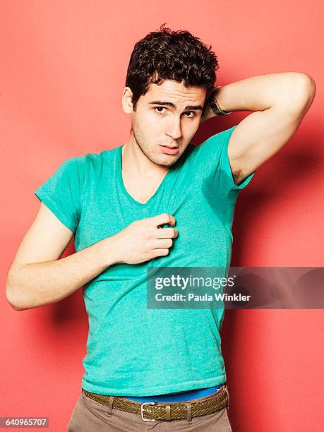 portrait of tired man showing sweaty t-shirt against red background - oksel stockfoto's en -beelden