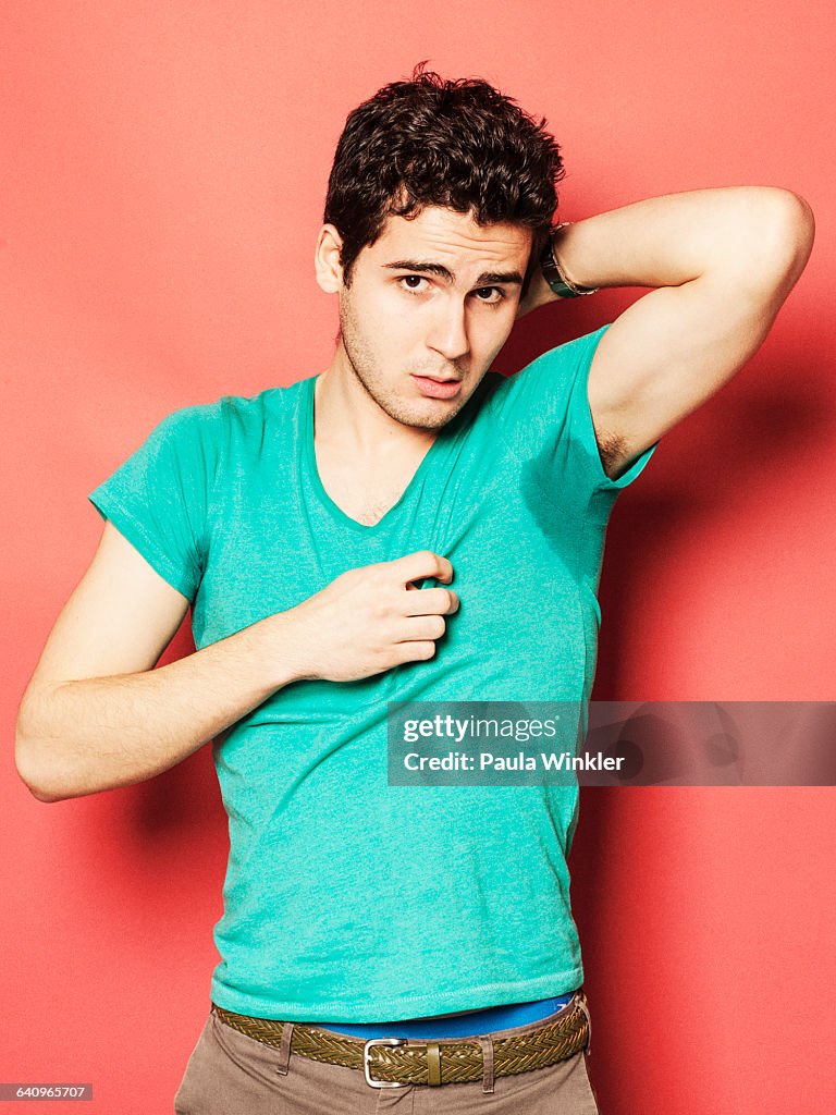 Portrait of tired man showing sweaty t-shirt against red background