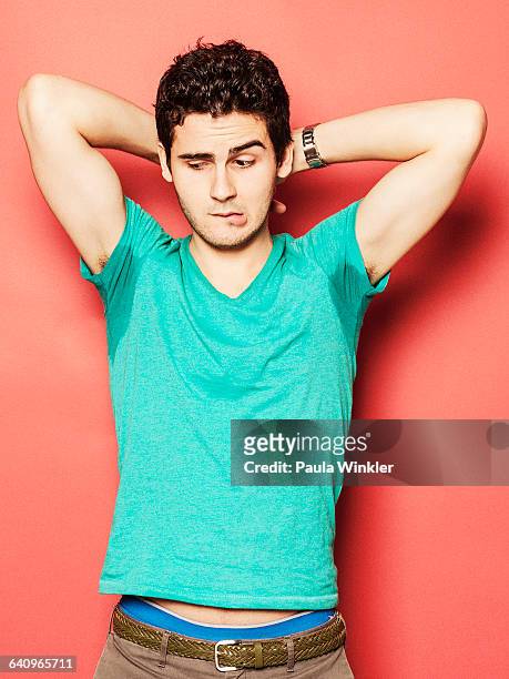 young man biting lip while looking at sweaty armpit against red background - nase rümpfen stock-fotos und bilder