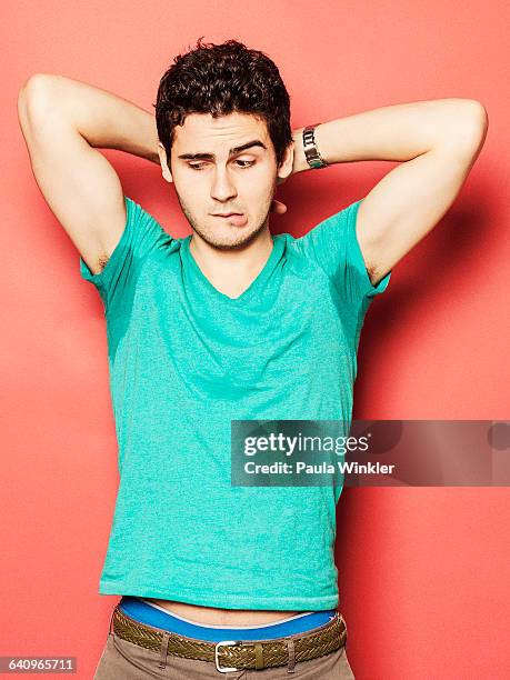 young man biting lip while looking at sweaty armpit against red background - olor desagradable fotografías e imágenes de stock