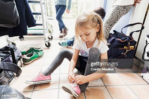 girl wearing shoe while sitting on floor at day care center - boy tying shoes stock pictures, royalty-free photos & images