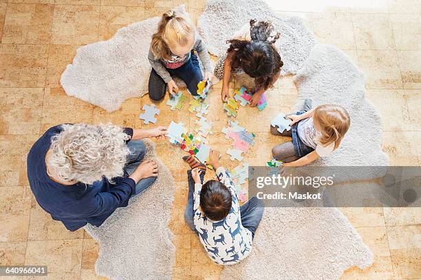 high angle view of teacher and children playing jigsaw puzzle - childhood development stock pictures, royalty-free photos & images