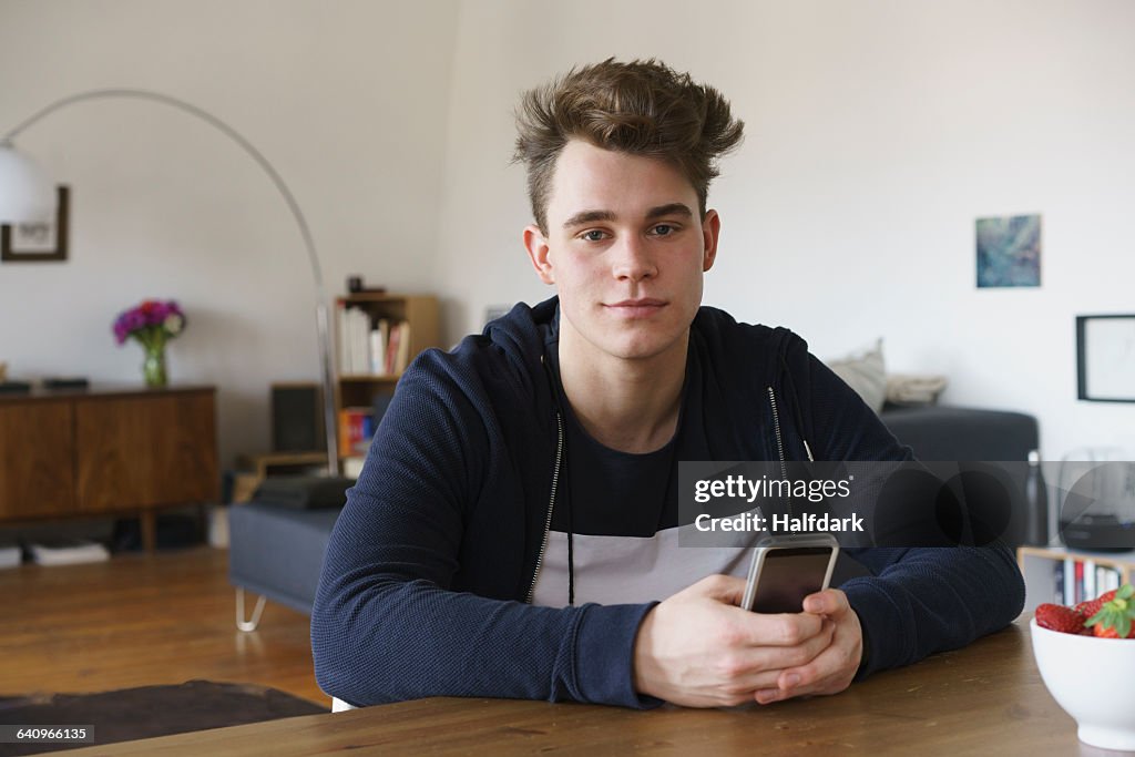 Portrait of teenage boy sitting at table with smart phone