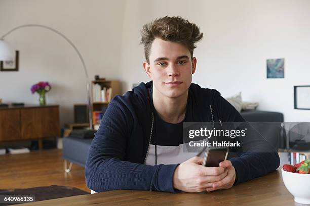 portrait of teenage boy sitting at table with smart phone - teenage boys stock pictures, royalty-free photos & images