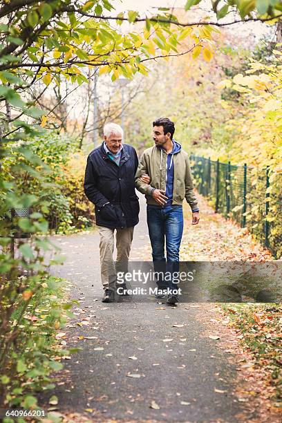 full length of happy senior man with caretaker walking in park - full frontal stock-fotos und bilder