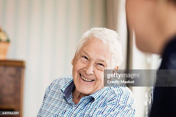 happy senior man looking at caretaker in nursing home - arbeiten pflege senior stock-fotos und bilder