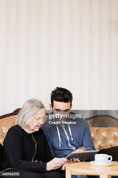 caretaker and senior woman using digital tablet while sitting on sofa at nursing home - volunteer aged care stock pictures, royalty-free photos & images