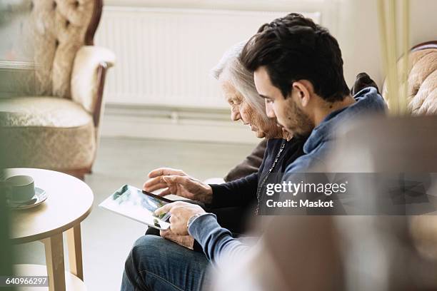 caretaker and senior woman using digital tablet at nursing home - old woman young man fotografías e imágenes de stock