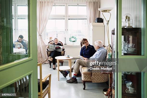 caretakers with senior couple sitting in living room at nursing home - paper furniture stockfoto's en -beelden