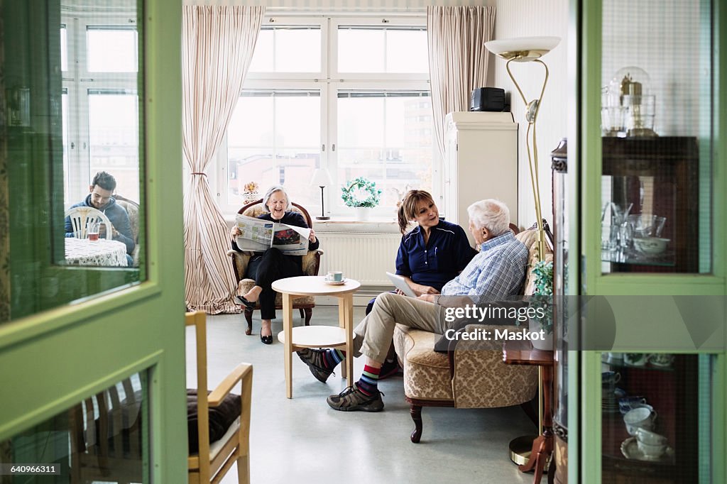 Caretakers with senior couple sitting in living room at nursing home