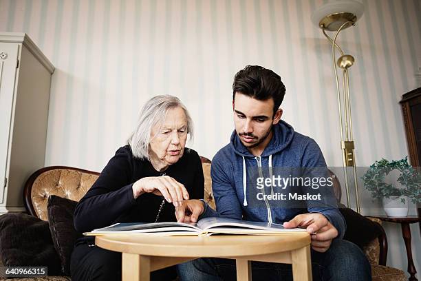 caretaker and senior woman discussing while reading book at nursing home - coffee table books stockfoto's en -beelden