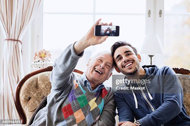 happy senior man taking selfie with caretaker through smart phone at nursing home - volunteer home care stock pictures, royalty-free photos & images