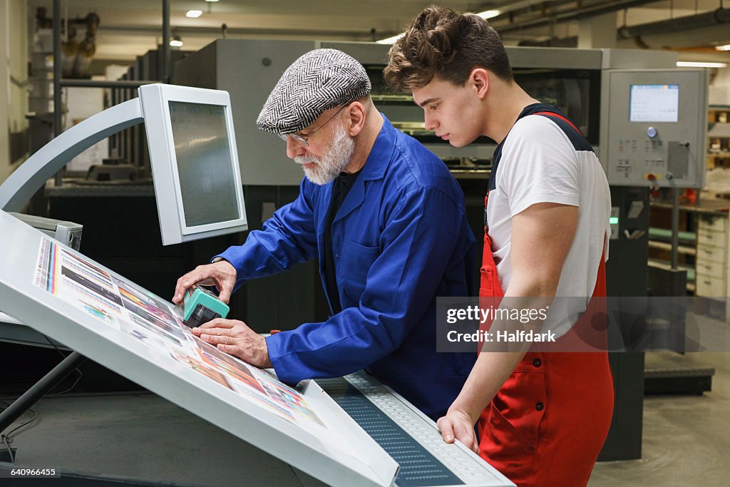 Young worker looking at mature colleague doing quality check of printout with scanner