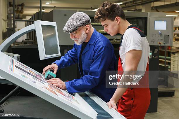 young worker looking at mature colleague doing quality check of printout with scanner - boy in briefs photos et images de collection