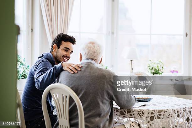 happy caretaker communicating to senior man in nursing home - senior patient stock-fotos und bilder