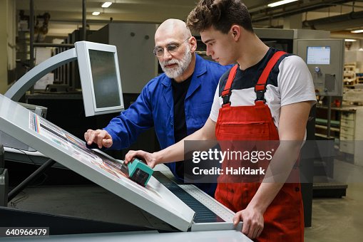 Mature Man And Coworker Doing Quality Check Of Printout With Machinery ...