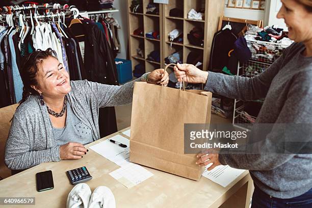 happy cashier giving shopping bag to customer in clothing store - disability collection stock pictures, royalty-free photos & images