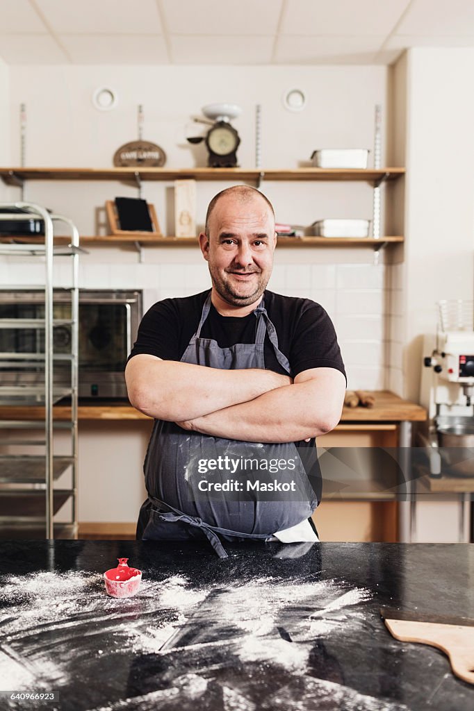 Portrait of man with arms crossed standing by table in kitchen