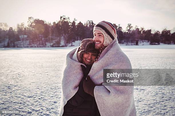 smiling couple wrapped in blanket while standing on field during winter - wrapped in a blanket stock pictures, royalty-free photos & images