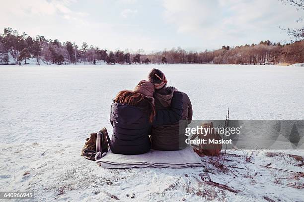 rear view of male and female hiker sitting on snow covered field - winter coat stock pictures, royalty-free photos & images