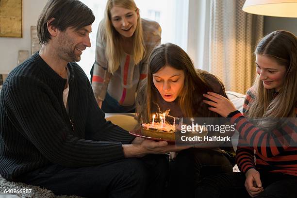 family looking at young woman blowing out birthday candles at home - daughter birthday stock pictures, royalty-free photos & images