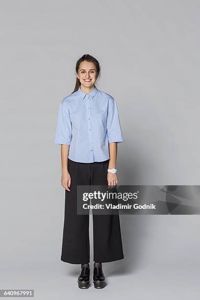 full length portrait of smiling woman standing against gray background - chignon stock pictures, royalty-free photos & images