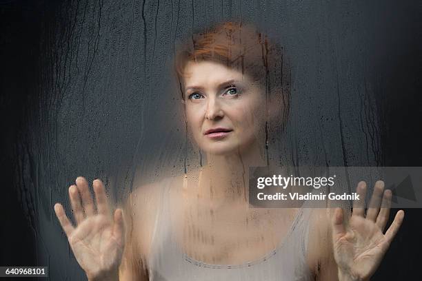 thoughtful beautiful woman standing in front on condensed glass against black background - brume fond noir photos et images de collection