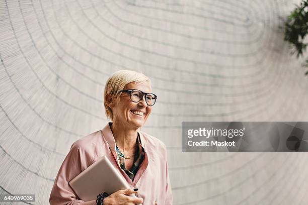 happy businesswoman holding digital tablet against wall in creative office - holding laptop stock pictures, royalty-free photos & images