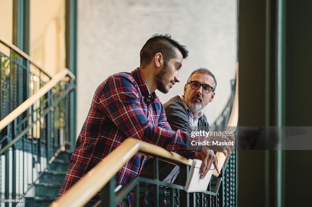 Mature businessman discussing with coworker on staircase in office