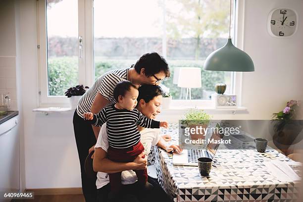 lesbian couple with daughter looking in laptop at kitchen - familie laptop stock-fotos und bilder