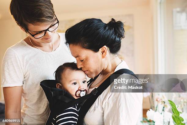 Woman looking at mother kissing baby girl while standing at home