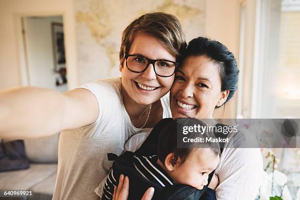 portrait of smiling lesbian couple with baby girl standing at home - lesbicas fotografías e imágenes de stock