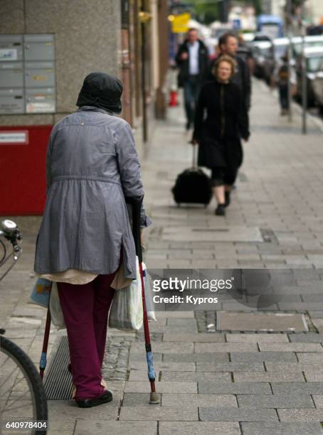 europe, germany, munich, view of elderly woman standing on pavement with crutches and plastic shopping bags - beggar stock-fotos und bilder