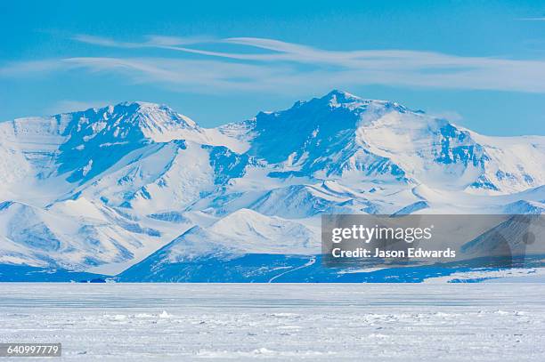 an enormous mountain range rises above the flat plain of sea ice. - antartide foto e immagini stock