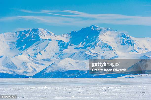 an enormous mountain range rises above the flat plain of sea ice. - polar stock pictures, royalty-free photos & images