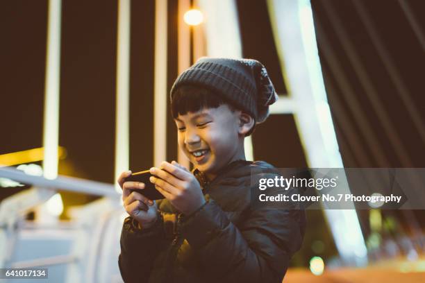 asian little boy using a smartphone in the street at night. - kid in winter coat stock pictures, royalty-free photos & images