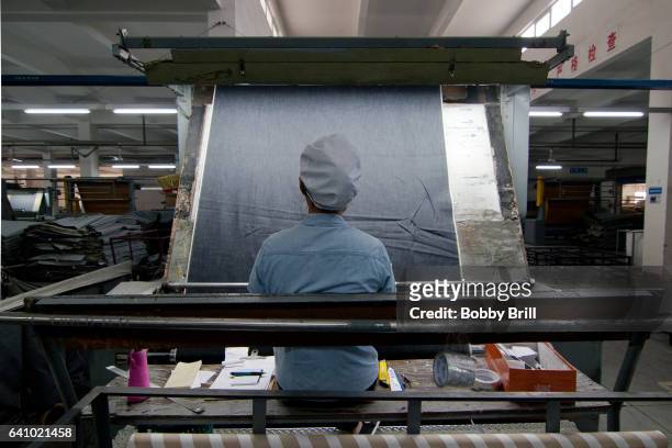 chinese worker examines denim fabric in a factory - sweatshop stock-fotos und bilder