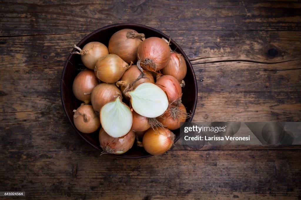 Onions in a wooden bowl on dark wood